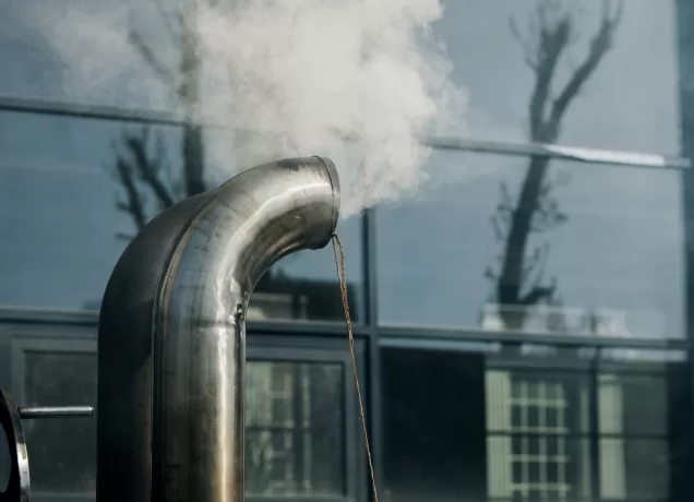 Tubo de sistema de exaustão liberando vapor, representando o funcionamento de sistemas de exaustão para controle de poeira metálica.